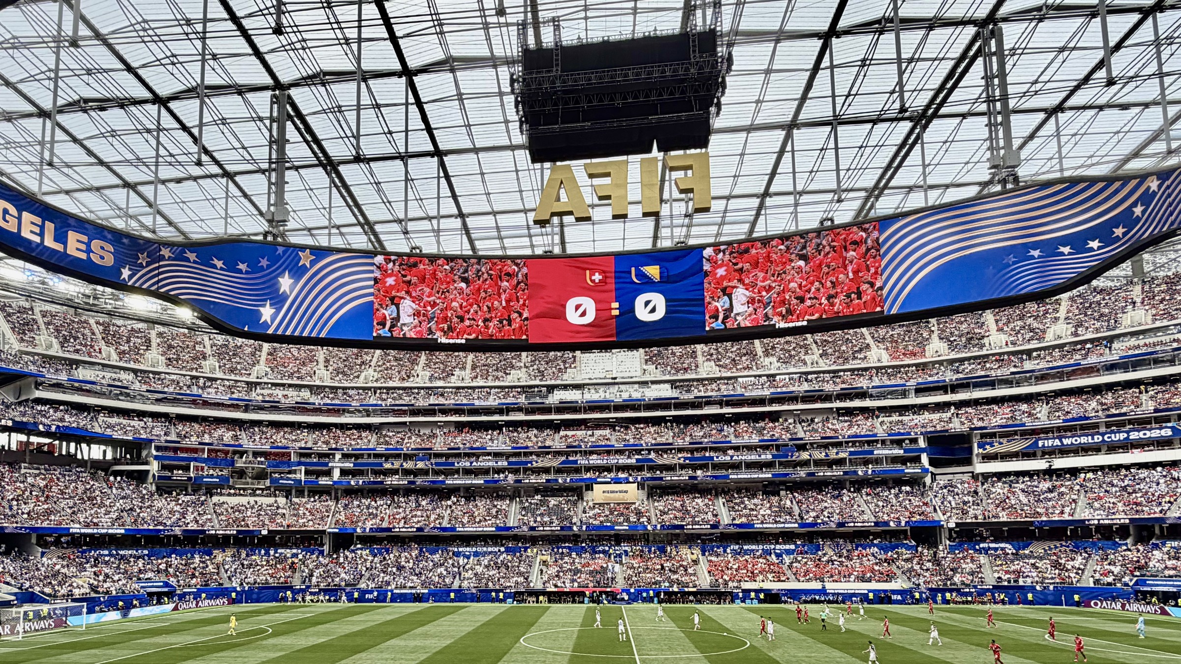 Wide view of SoFi Stadium during a 2026 FIFA World Cup group stage match between Switzerland and Bosnia and Herzegovina, the scoreboard reading 0-0 above a packed crowd.